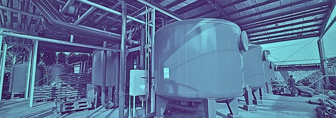 Instalasi pengolahan air bersih hasil dari proyek jasa EPC water treatment, menunjukkan tangki-tangki filter besar dan sistem perpipaan yang terpasang rapi di dalam sebuah pabrik.