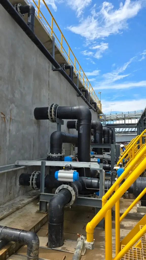 Close-up of the advanced piping system and automated control valves at the GLS SWRO desalination plant, showing the robust engineering supporting the water treatment process against a clear blue sky.