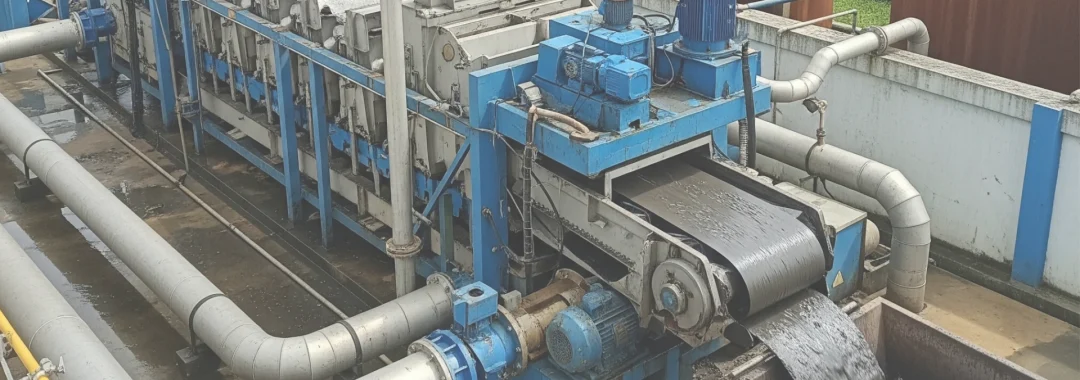 Industrial sludge dewatering equipment in action, processing wastewater sludge into a dry cake at a treatment facility in Indonesia.